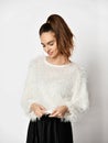 Young beautiful shy brunette woman in white fur sweater and pleated skirt is looking down in the corner