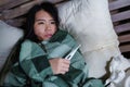 Young beautiful sick and exhausted Asian Korean woman suffering cold and flu holding thermometer having temperature lying on bed Royalty Free Stock Photo