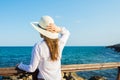 Young beautiful slender woman with long hair holding sunhat from wind in boho style clothes at the shore looking and the sea Royalty Free Stock Photo