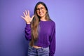 Young beautiful smart woman wearing glasses over purple isolated background showing and pointing up with fingers number five while