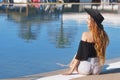 Young beautiful smile girl in black fashion hat, red lips and long hair, posing near pool beackground of palms.