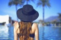 Young beautiful smile girl in black fashion hat, red lips and long hair, posing near pool beackground of palms. Royalty Free Stock Photo