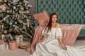 Young beautiful smile woman in white elegant evening dress sitting on floor near christmas tree and presents. Interior with christ Royalty Free Stock Photo