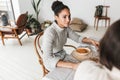 Young beautiful smiling african american woman with dark curly hair sitting at the table dreamily looking aside while Royalty Free Stock Photo