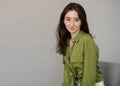 Young beautiful smiling brunette woman in a green blouse sitting in a chair against a gray wall looking at the camera Royalty Free Stock Photo