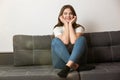 Young beautiful smiling brunette woman sitting on the sofa in her appartment holding hands near face looking happy Royalty Free Stock Photo