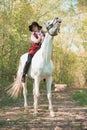 Brunette woman riding dark horse at summer green forest. Royalty Free Stock Photo