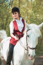 Brunette woman riding dark horse at summer green forest. Royalty Free Stock Photo