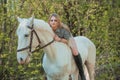 Brunette woman riding dark horse at summer green forest. Royalty Free Stock Photo