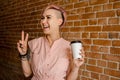 Young beautiful smiling girl holds paper cup of coffee on a brick wall background Royalty Free Stock Photo