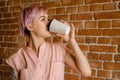 Young beautiful smiling girl holds paper cup of coffee on a brick wall background Royalty Free Stock Photo