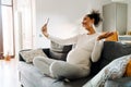 Young beautiful smiling pregnant afro woman sitting sofa taking selfie Royalty Free Stock Photo