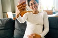 Young beautiful smiling pregnant afro woman sitting sofa taking selfie Royalty Free Stock Photo