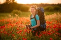 Young beautiful smiling woman with backpack and walking sticks stands on field of poppies Royalty Free Stock Photo