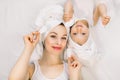 Young beautiful smiling woman and her pretty little daughter with towels on their heads, lying together on the bed and Royalty Free Stock Photo