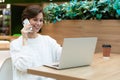 Young beautiful smiling woman sitting at a shopping center at a table and working at a computer laptop, using mobile Royalty Free Stock Photo