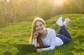 Young beautiful woman student with a laptop lies on the grass in sunset Royalty Free Stock Photo