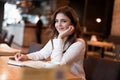 Young beautiful smiling woman in white jacket taking notes to her planner working outside office drinking hot coffee in the trendy Royalty Free Stock Photo