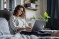 Young beautiful smiling woman working on business project using laptop while sitting in bed at home Royalty Free Stock Photo