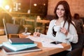 Young beautiful smiling woman working outside office in her laptop taking notes in her notebook while drinking hot coffee in the Royalty Free Stock Photo