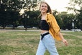 Young beautiful smiling woman in yellow shirt and jeans happily walking on lawn in park