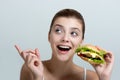 Young beautiful smilling girl holds a burger in hand and pointing to the left side