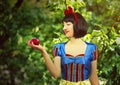 Young beautiful snow-white close-up keeps a red poisoned apple against the background of trees in the forest