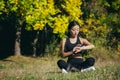 Young beautiful sports girl asian woman meditating in park, sitting lotus pose practicing yoga mat outdoors looking smart watch at Royalty Free Stock Photo