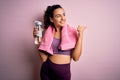 Young beautiful sportswoman with curly hair doing sport drinking bottle of water using towel pointing and showing with thumb up to