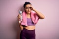 Young beautiful sportswoman with curly hair doing sport drinking bottle of water using towel stressed with hand on head, shocked Royalty Free Stock Photo