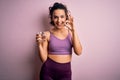 Young beautiful sportswoman with curly hair doing sport drinking glass of water doing ok sign with fingers, excellent symbol