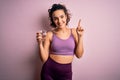 Young beautiful sportswoman with curly hair doing sport drinking glass of water surprised with an idea or question pointing finger