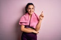 Young beautiful sportswoman with curly hair doing sport using towel over pink background with a big smile on face, pointing with