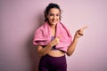 Young beautiful sportswoman with curly hair doing sport using towel over pink background smiling and looking at the camera