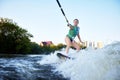 Young beautiful sporty girl in a green life jacket rides a wakeboard on a river or lake near city. Happy sportswoman Royalty Free Stock Photo