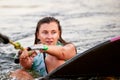 Young beautiful sporty girl in a green life jacket sitting in the water on a wakeboard with a halyard in her hand Royalty Free Stock Photo