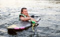 Young beautiful sporty girl in a green life jacket swims in the water with wakeboard and halyard in her hand. Happy Royalty Free Stock Photo