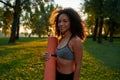 Young beautiful sporty mixed race woman wearing sport clothes holding yoga mat, looking at camera and smiling while Royalty Free Stock Photo