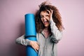 Young beautiful sporty woman with curly hair and piercing holding mat doing yoga with happy face smiling doing ok sign with hand