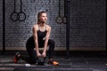 Young beautiful sporty woman holding kettlebell on the gym floor against brick wall.