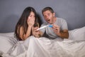 Young beautiful and stressed couple in bed looking pregnancy test feeling happy and surprised by positive pregnant result looking