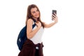 Young beautiful student girl with backpack makes selfie isolated on white background in studio Royalty Free Stock Photo