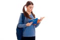 Young beautiful student girl with backpack reads a book and posing isolated on white background in studio Royalty Free Stock Photo