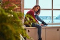 Young beautiful student girl sitting with laptop on window sill in student dormitory. Royalty Free Stock Photo