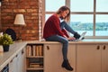 Young beautiful student girl sitting with laptop on window sill in student dormitory. Royalty Free Stock Photo