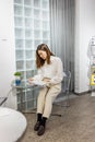 Young and beautiful stylish Asian woman sitting on chair and reading magazine in relax conner of modern office or cafe. Royalty Free Stock Photo