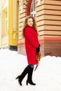 Young, beautiful and stylish blonde hair girl in red coat and with handbag walking through city streets. Womens fashion. Royalty Free Stock Photo