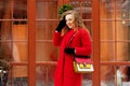 Young, beautiful and stylish blonde hair girl in red coat and with handbag walking through city streets. Womens fashion. Royalty Free Stock Photo