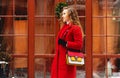 Young, beautiful and stylish blonde hair girl in red coat and with handbag walking through city streets. Womens fashion. Royalty Free Stock Photo