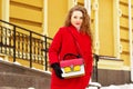 Young, beautiful and stylish blonde hair girl in red coat and with handbag walking through city streets. Womens fashion. Royalty Free Stock Photo